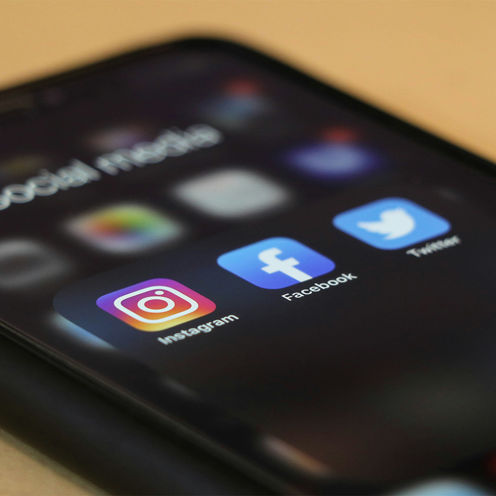 Partie d'un écran de téléphone portable affichant les logos de réseaux sociaux d'Instagram, de Facebook et de Twitter.